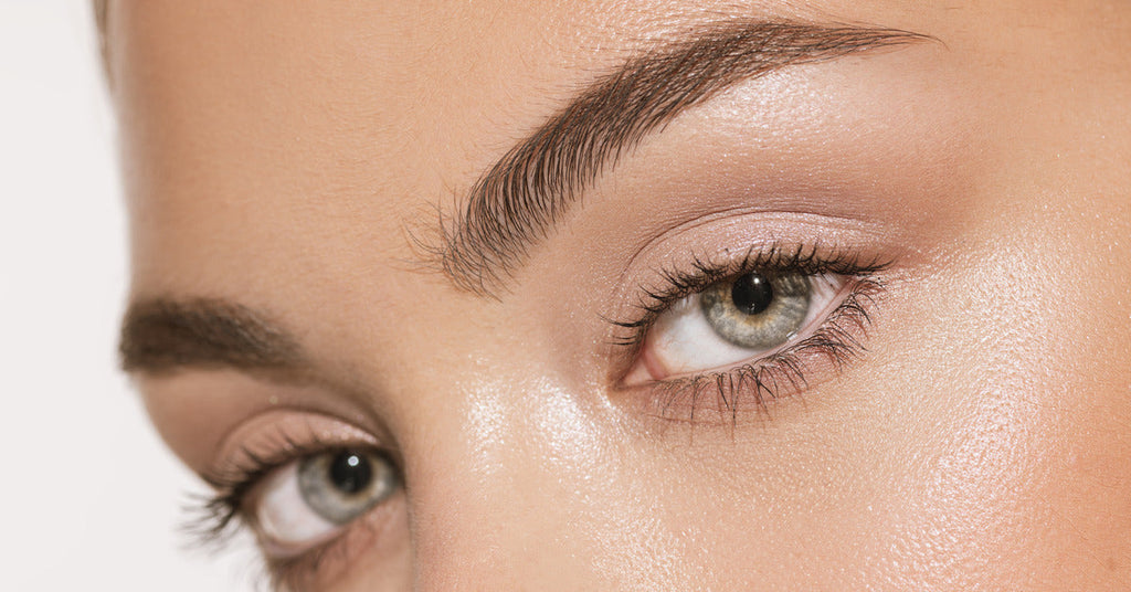 A close-up of a pair of gray-green eyes looking toward the camera. The person is wearing natural makeup.